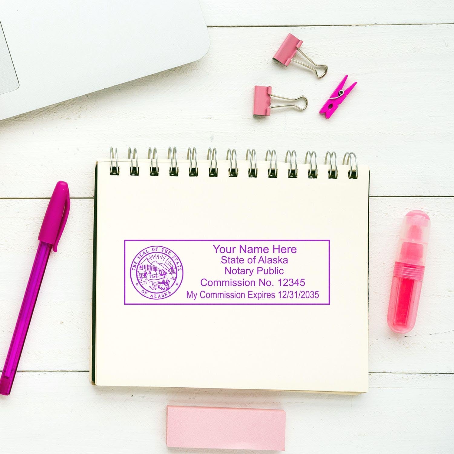 Notary Stamp Image: A notary public stamp from the State of Alaska on a spiral notebook, surrounded by pink office supplies.