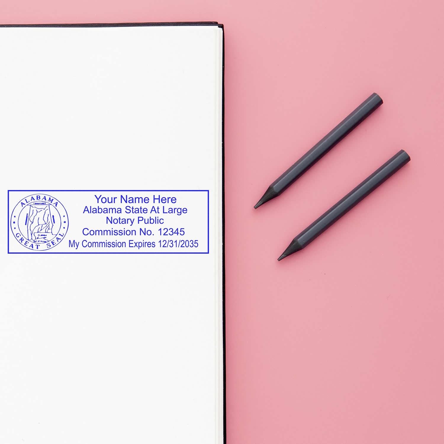 Image of an Alabama notary public stamp on a white page with two pens on a pink background. Alabama Notary Supplies Blog Post Feature Image.