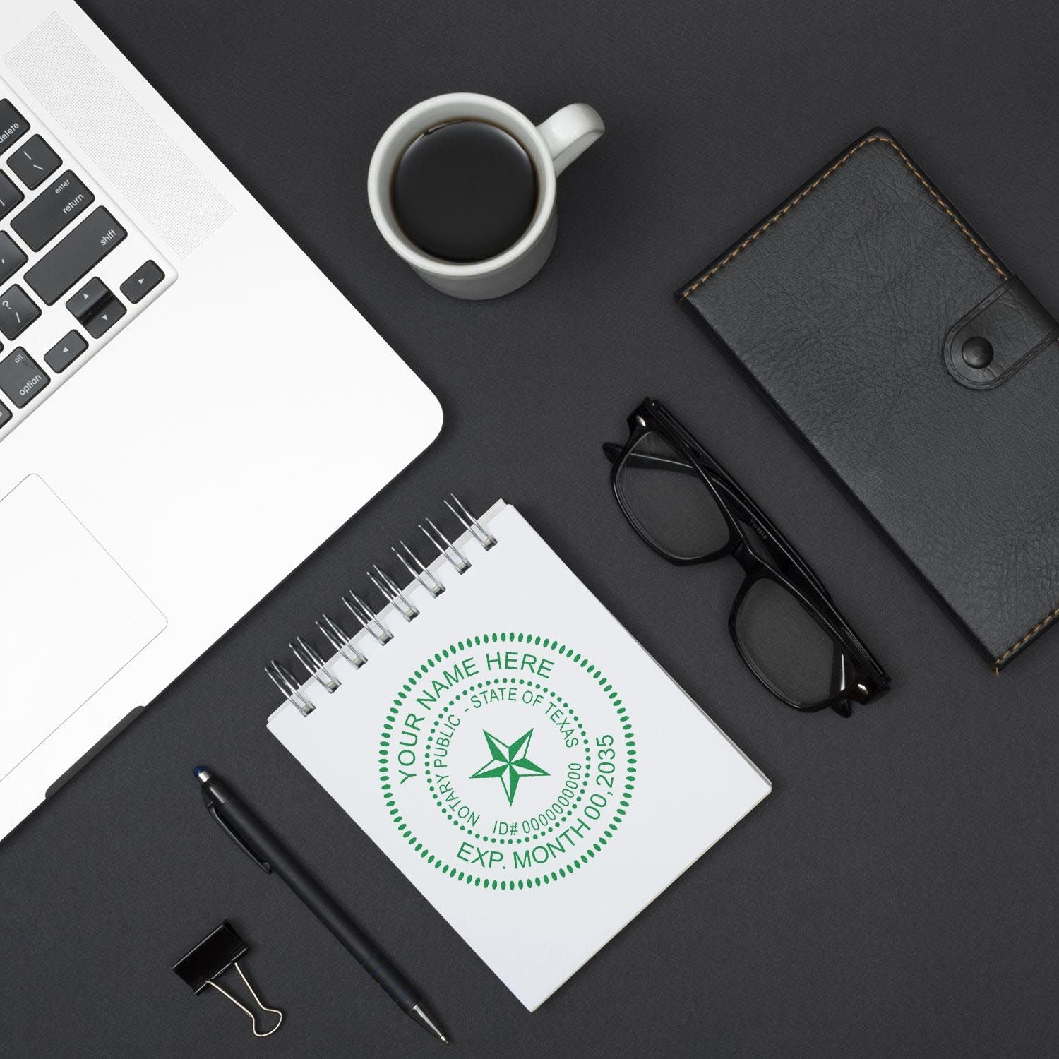 Alt Text: Texas Notary Supplies Blog Post Feature Image: A notary stamp, notebook, pen, glasses, wallet, coffee, and laptop on a black desk.