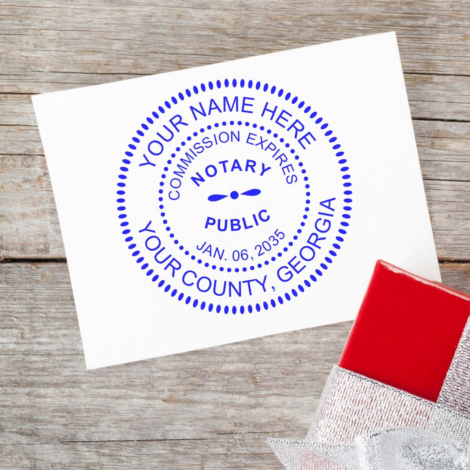 Notary seal on a white card with a red gift box on a wooden surface. Blog post: The Difference Between Notary Seals and Stamps Feature Post Image.