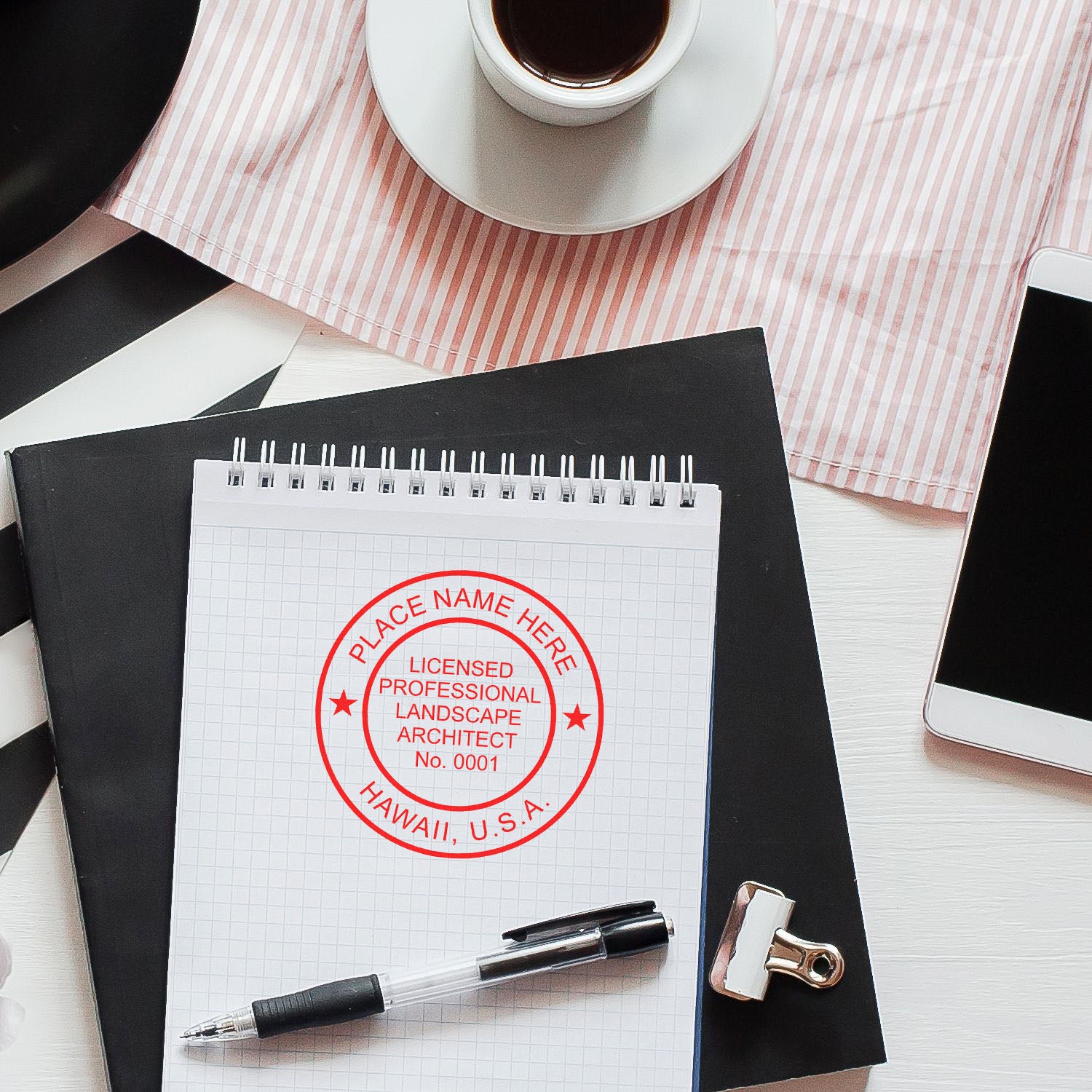 Hawaii Landscape Architect Feature Image: A desk with a coffee cup, phone, pen, and notepad displaying a red landscape architect seal stamp.