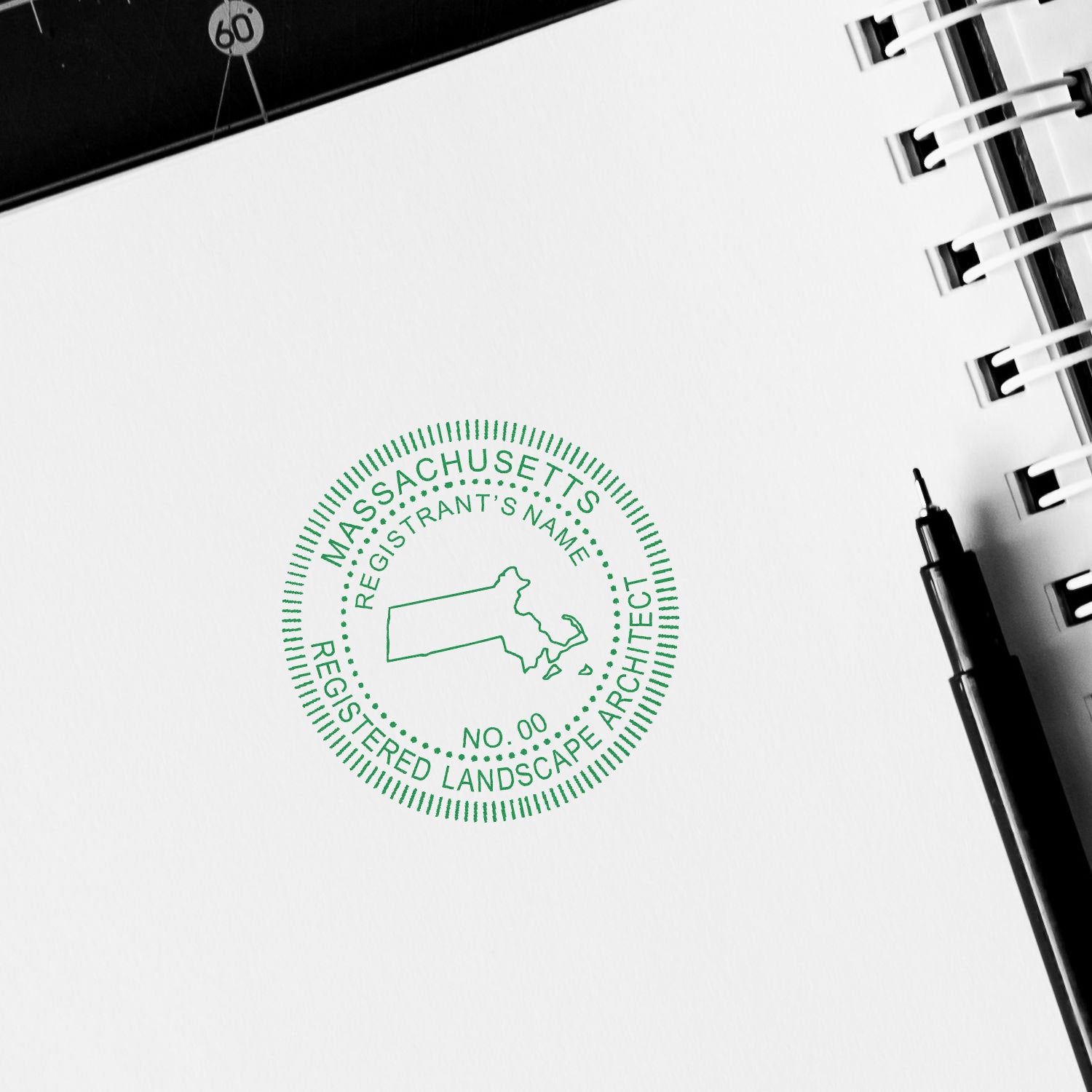 Massachusetts Landscape Architect Feature Image: Green seal stamp on white paper with a pen and notebook in the background.