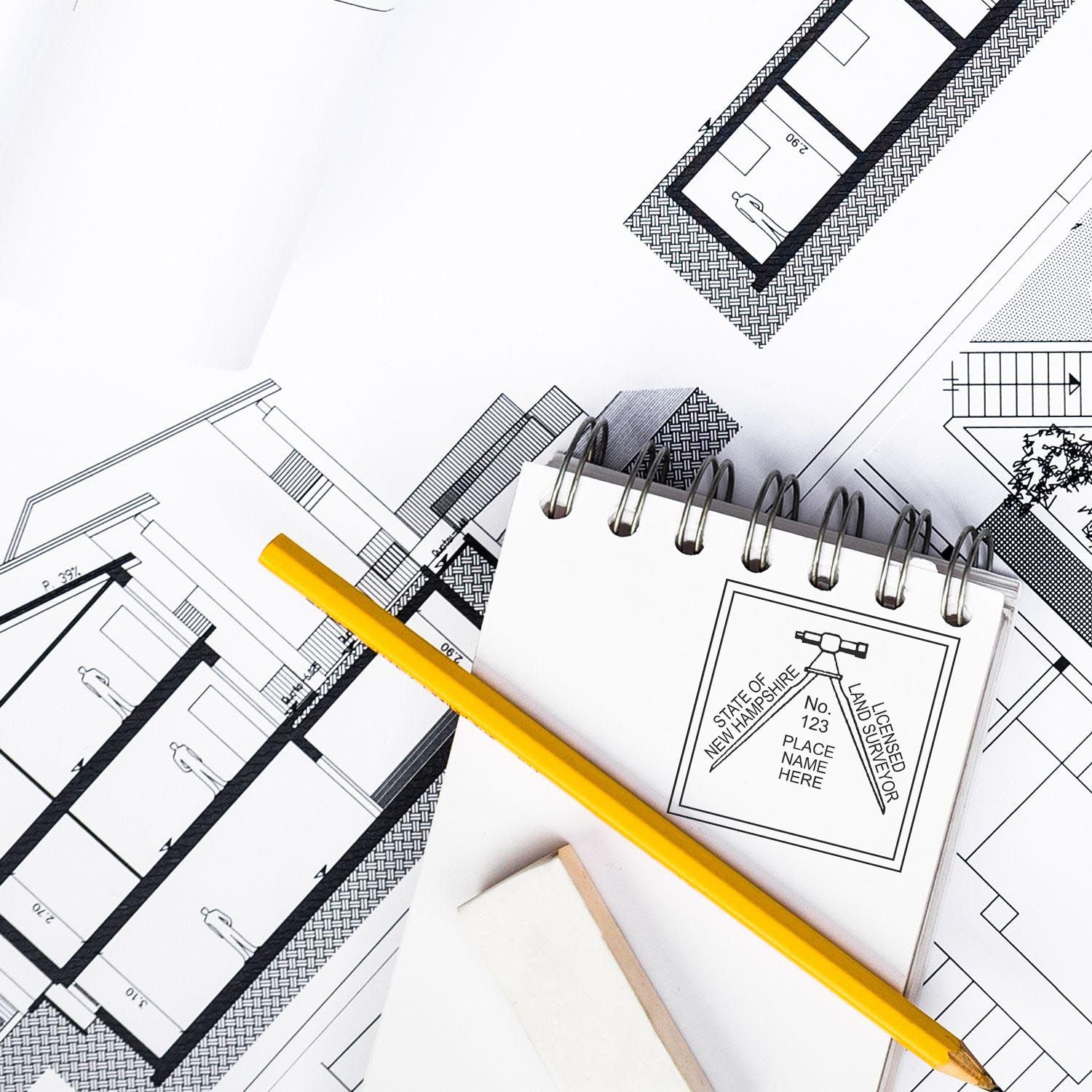 Blueprints, a yellow pencil, and a New Hampshire Land Surveyor Stamp on a notepad. Blog post: New Hampshire Land Surveyor Stamp.