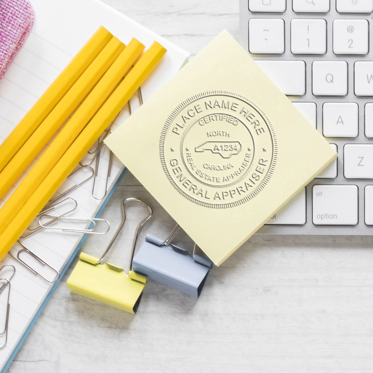 Real Estate Appraiser Embossed Seal image on a sticky note beside a keyboard, pencils, and paper clips.