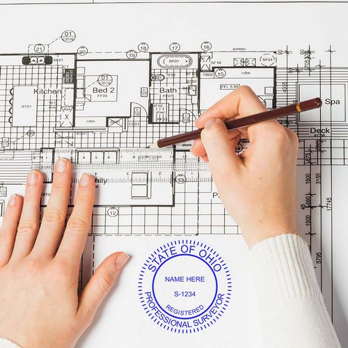 Person using Ohio Land Surveyor Stamp on architectural blueprint. Blog post: Ohio Land Surveyor Stamp.