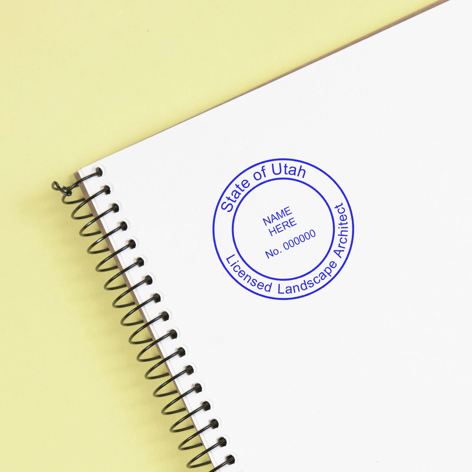 Utah Landscape Architect Feature Image: A spiral notebook with a blue 'State of Utah Licensed Landscape Architect' seal stamp on a yellow background.