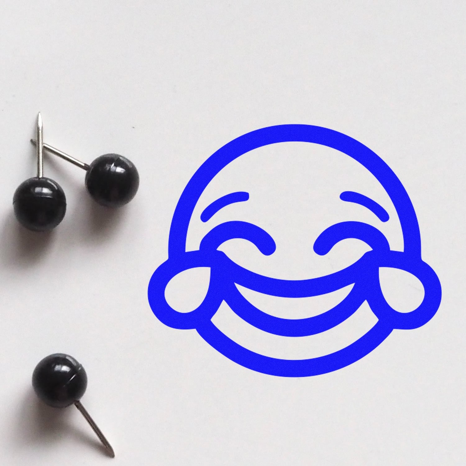 Self-Inking Cheeky Grin Emoji Stamp on white paper, featuring a bold blue smiling face with blushing cheeks. Perfect for adding a playful touch to notes and crafts.