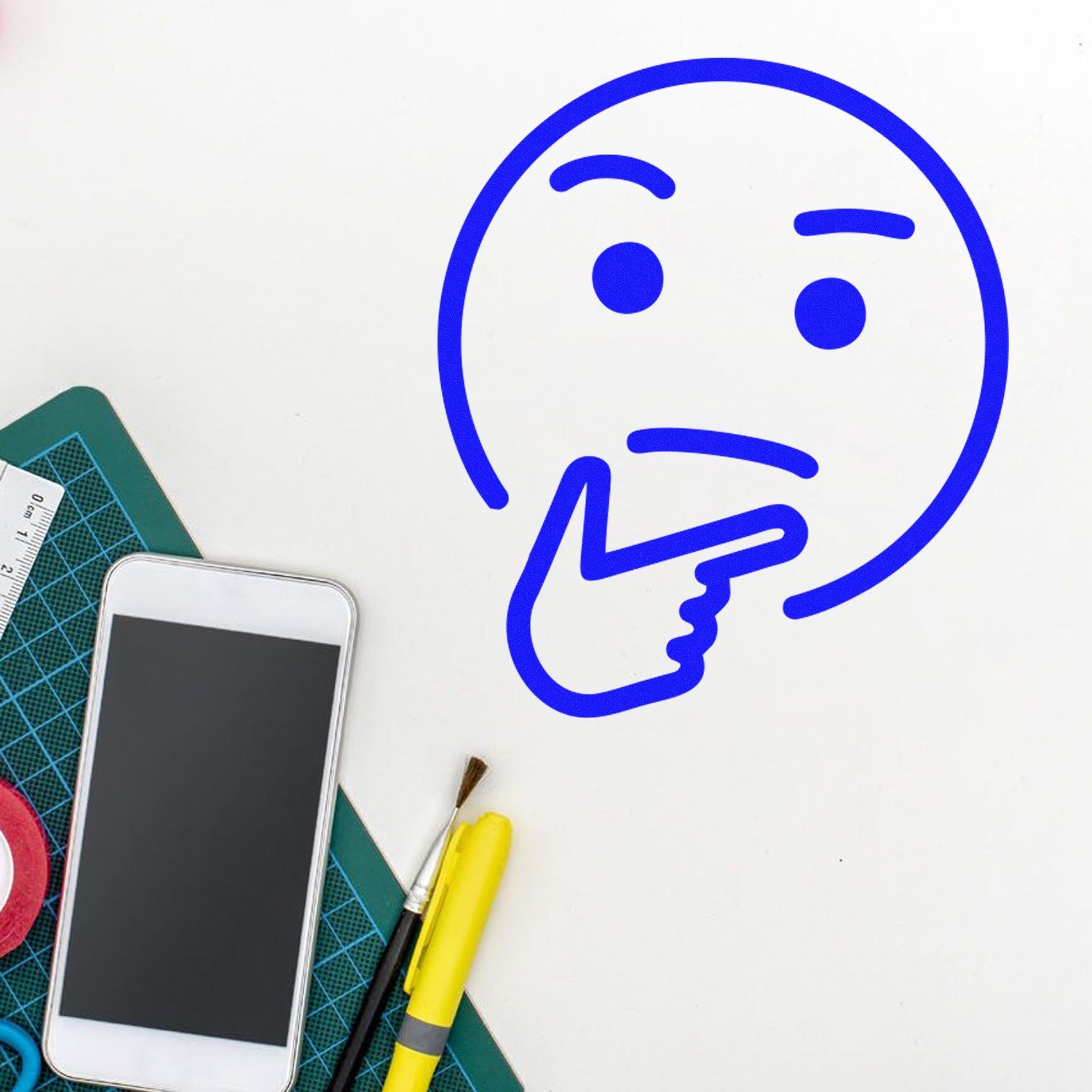 Self-Inking Pondering Pete Emoji Stamp in use, featuring a blue pondering face design on white paper, next to a smartphone and stationery items.