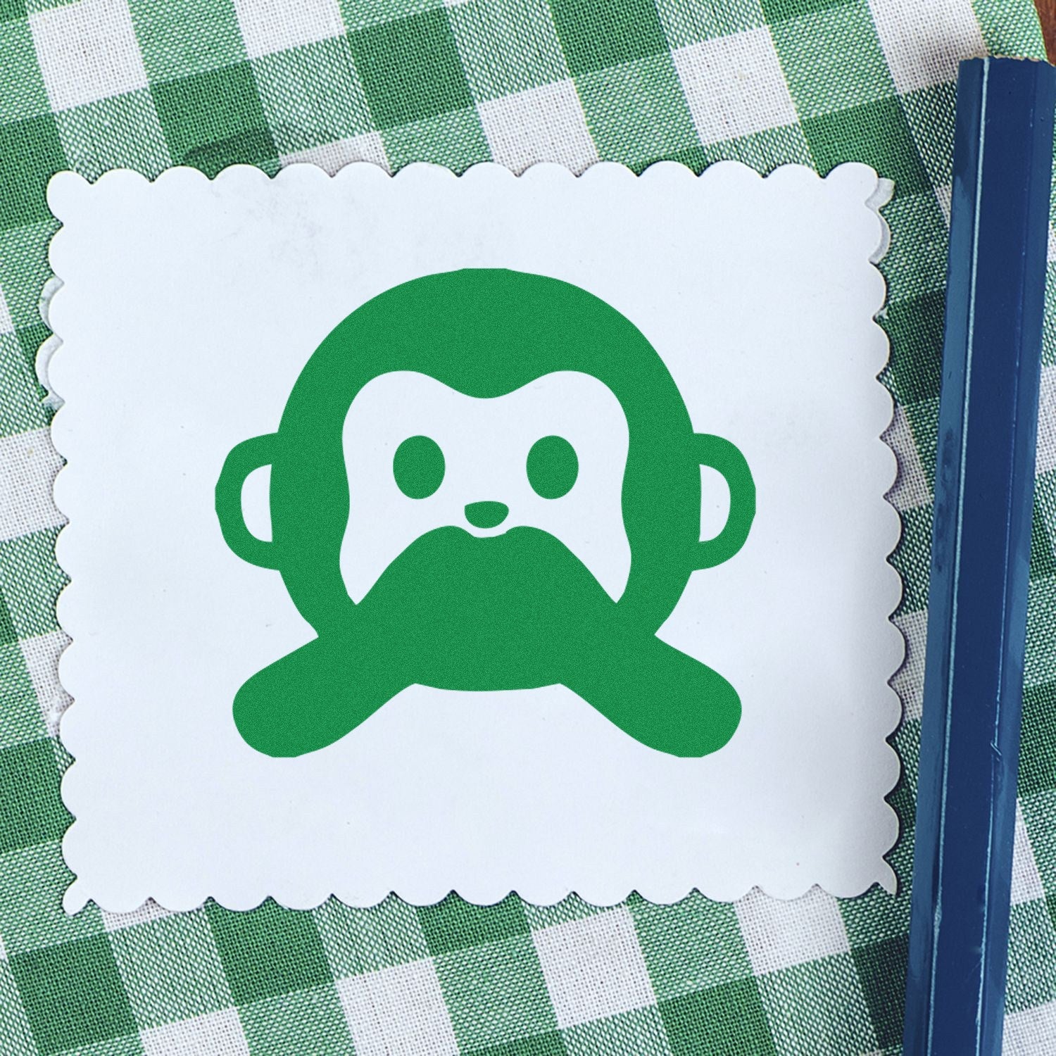 Image of a Self-Inking Mute Monkey Facial Expressions Stamp on a green checkered tablecloth, featuring a cute green monkey design with a scalloped edge card. Perfect for crafting and stationery.