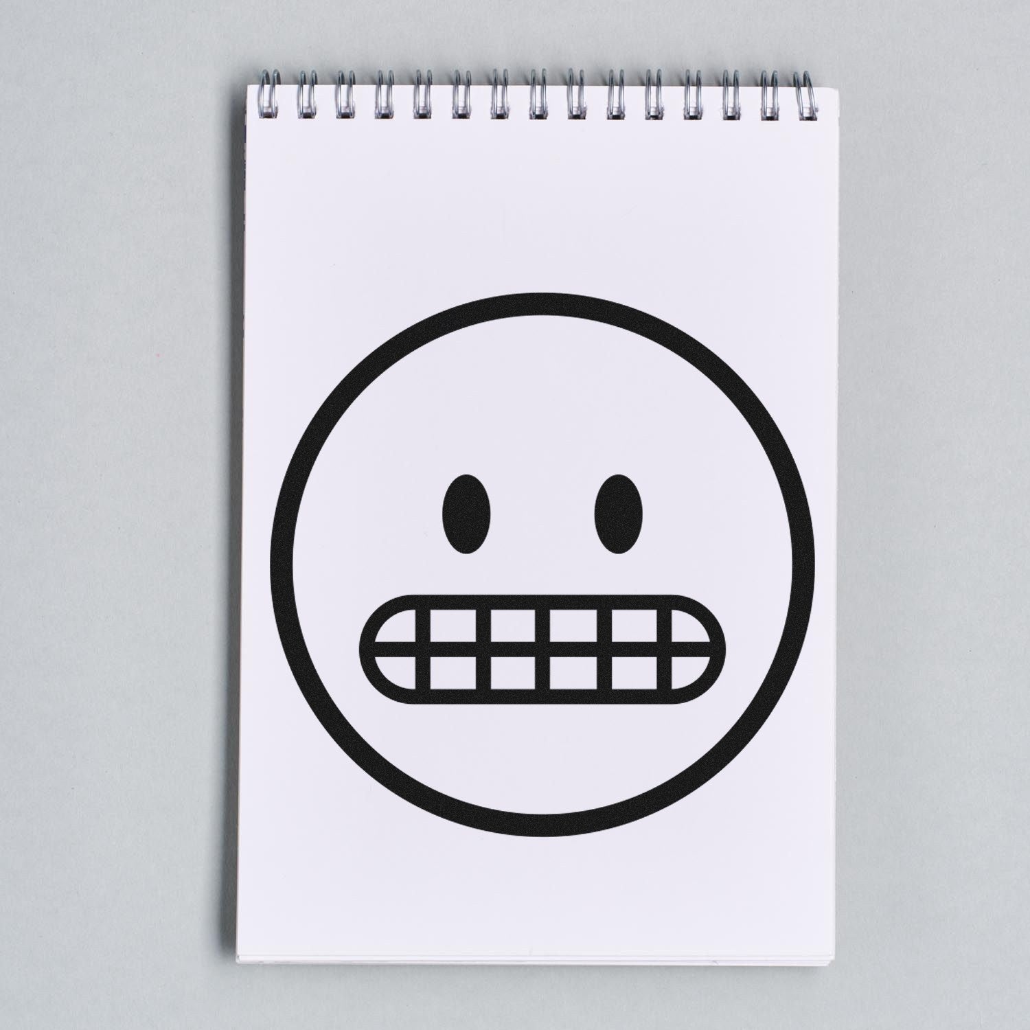 Wood Handle Awkward Alan Emoji Rubber Stamp featuring a quirky, gritted teeth emoji design on a spiral notebook. Perfect for adding personality to crafts and stationery.