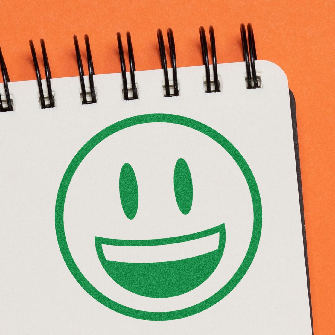 Wood Handle Grinning Delight Emoji Rubber Stamp on orange background, featuring a green smiling face imprint on white paper. Perfect for adding a cheerful touch to crafts and stationery.