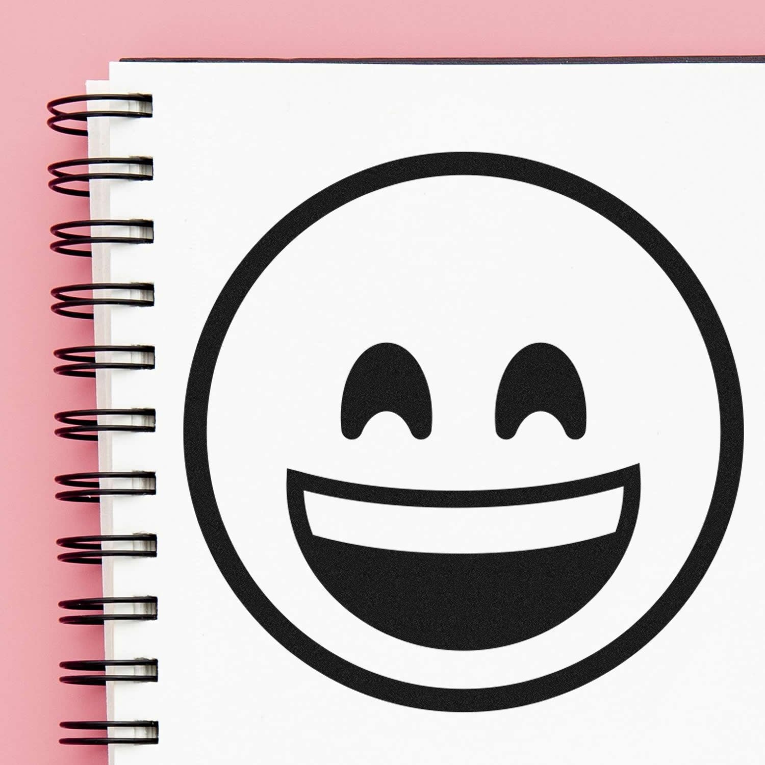 Wood Handle Ecstatic Eyes Emoji Rubber Stamp on a spiral notebook, featuring a joyful emoji design. Perfect for adding fun to crafts and stationery.