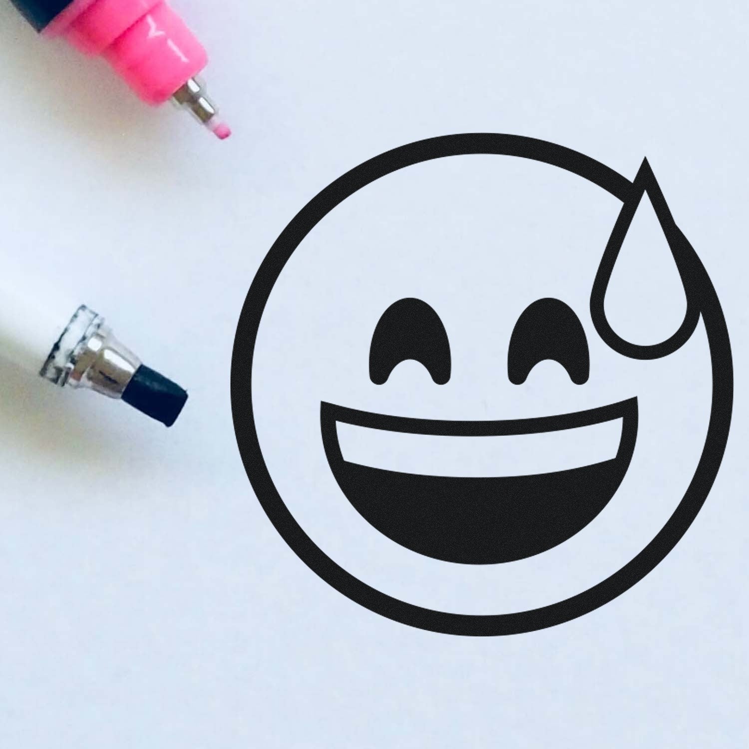 Wood Handle Blushing Chuckles Emoji Rubber Stamp on white paper, featuring a smiling emoji with a sweat drop. Includes a pink and black marker nearby for size reference. Perfect for crafts and stationery.