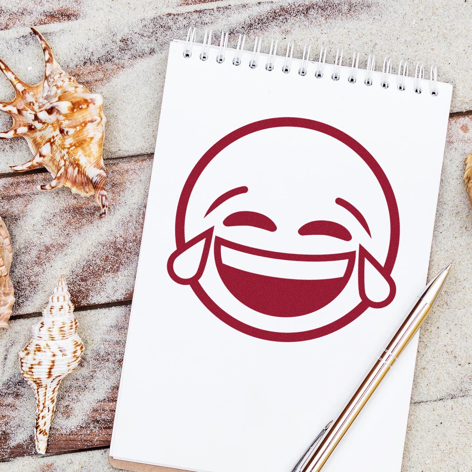 Wood Handle Tearful Giggles Emoji Rubber Stamp on a notepad, showcasing a laughing emoji with tears. Perfect for adding a playful touch to crafts and stationery.