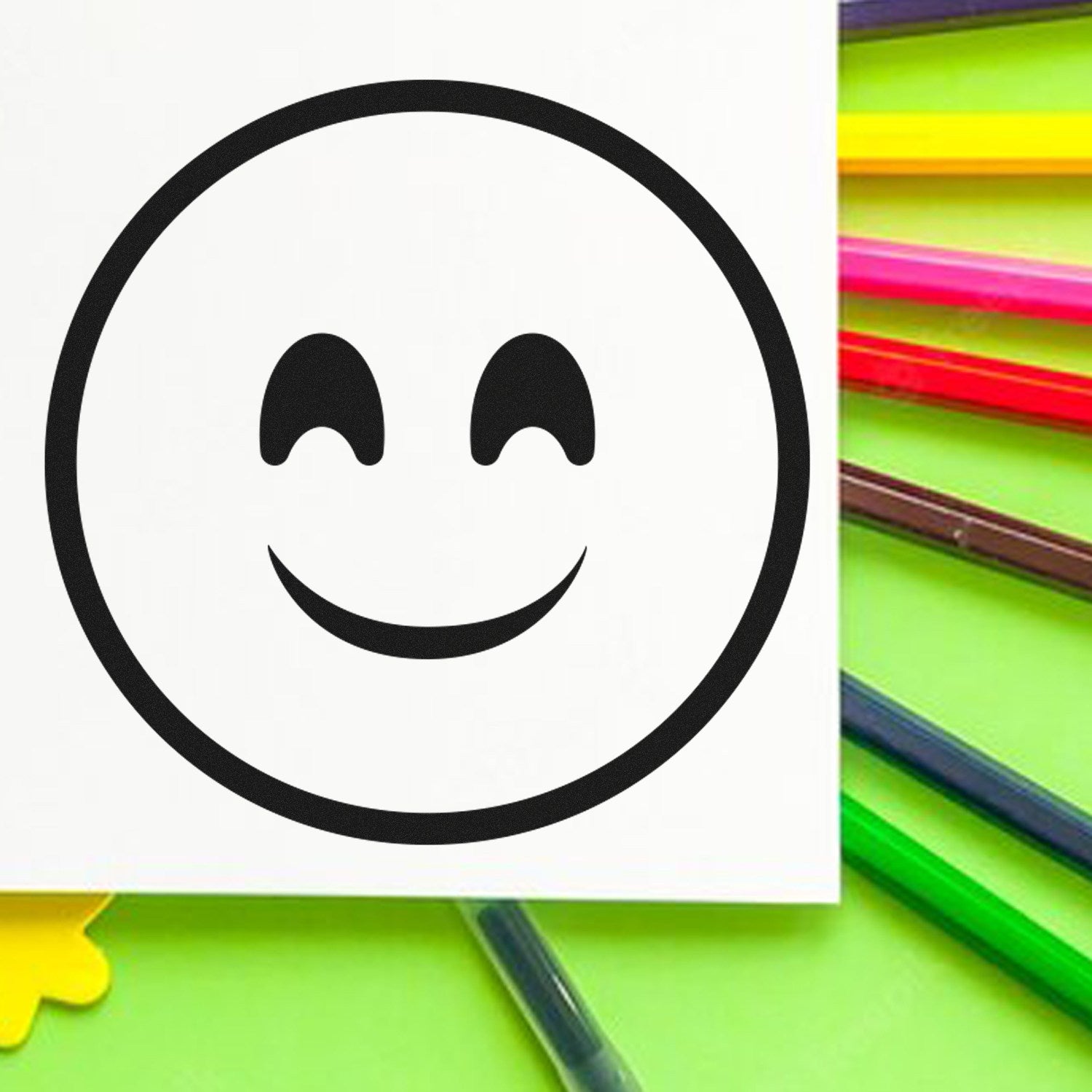 Self-Inking Blissful Wink Emoji Stamp on paper with colorful pens, featuring a smiling wink emoji design. Perfect for adding fun to notes and crafts.