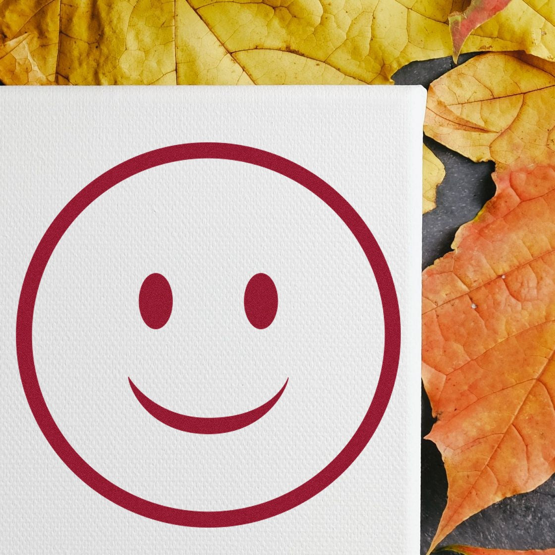 Wood Handle Simple Smiley Emoji Rubber Stamp on a canvas, surrounded by vibrant autumn leaves. Perfect for adding a cheerful touch to crafts and stationery.