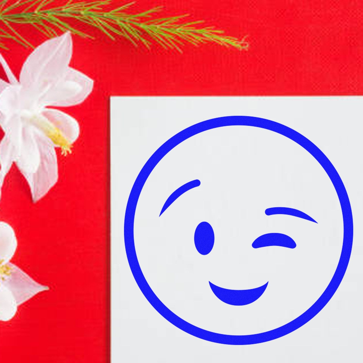 Image of a Self-Inking Winky Face Pictogram Stamp on white paper, featuring a blue winky face design. The stamp is set against a vibrant red background with white flowers.