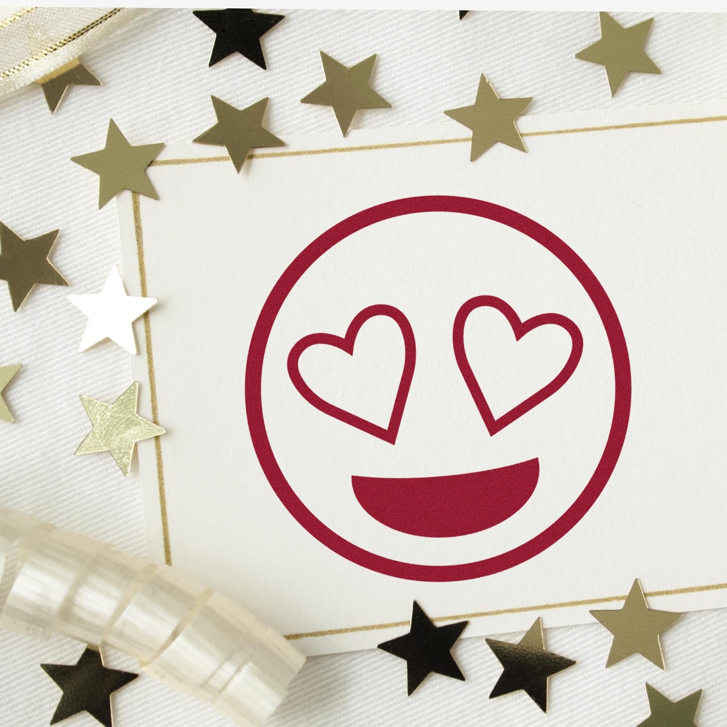 Wood Handle Heart-Eyes Reaction Rubber Stamp on white paper, surrounded by gold stars and ribbon. Perfect for crafts and stationery, featuring a heart-eyes emoji design.