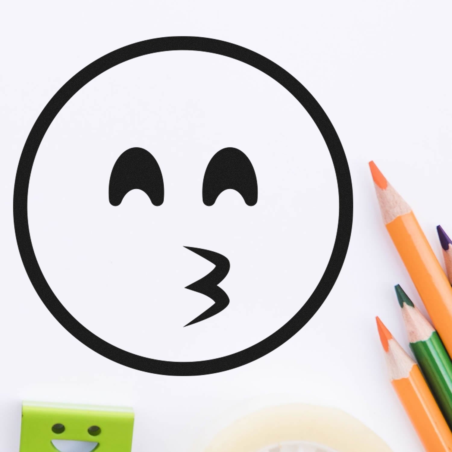 Self-Inking Whistling Wendy Emoji Stamp on white paper, featuring a playful whistling face. Includes colorful pencils and stationery, perfect for adding fun to crafts and documents.