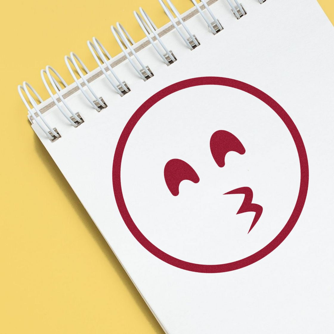 Self-Inking Whistling Wendy Emoji Stamp on a notepad, featuring a red whistling face design. Perfect for adding fun, expressive touches to your notes and crafts.