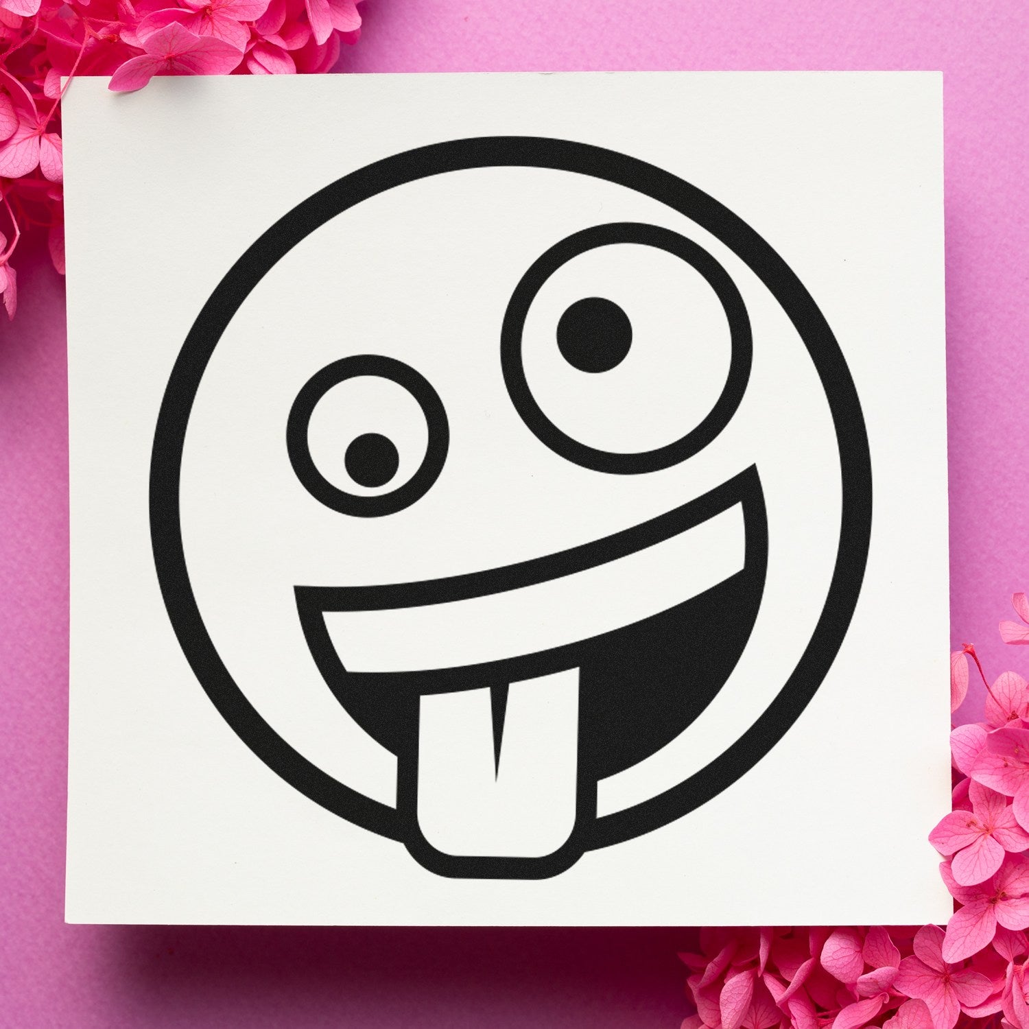 Wood Handle Zany Grin Emoji Rubber Stamp on pink background with flowers, featuring a playful emoji with a wide grin and tongue out. Perfect for adding fun to crafts and stationery.