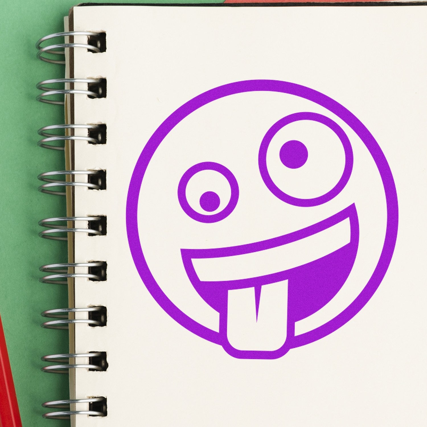 Self-Inking Zany Grin Emoji Stamp on a notebook page, featuring a playful purple emoji with a winking eye and tongue out. Perfect for adding fun to notes and crafts.