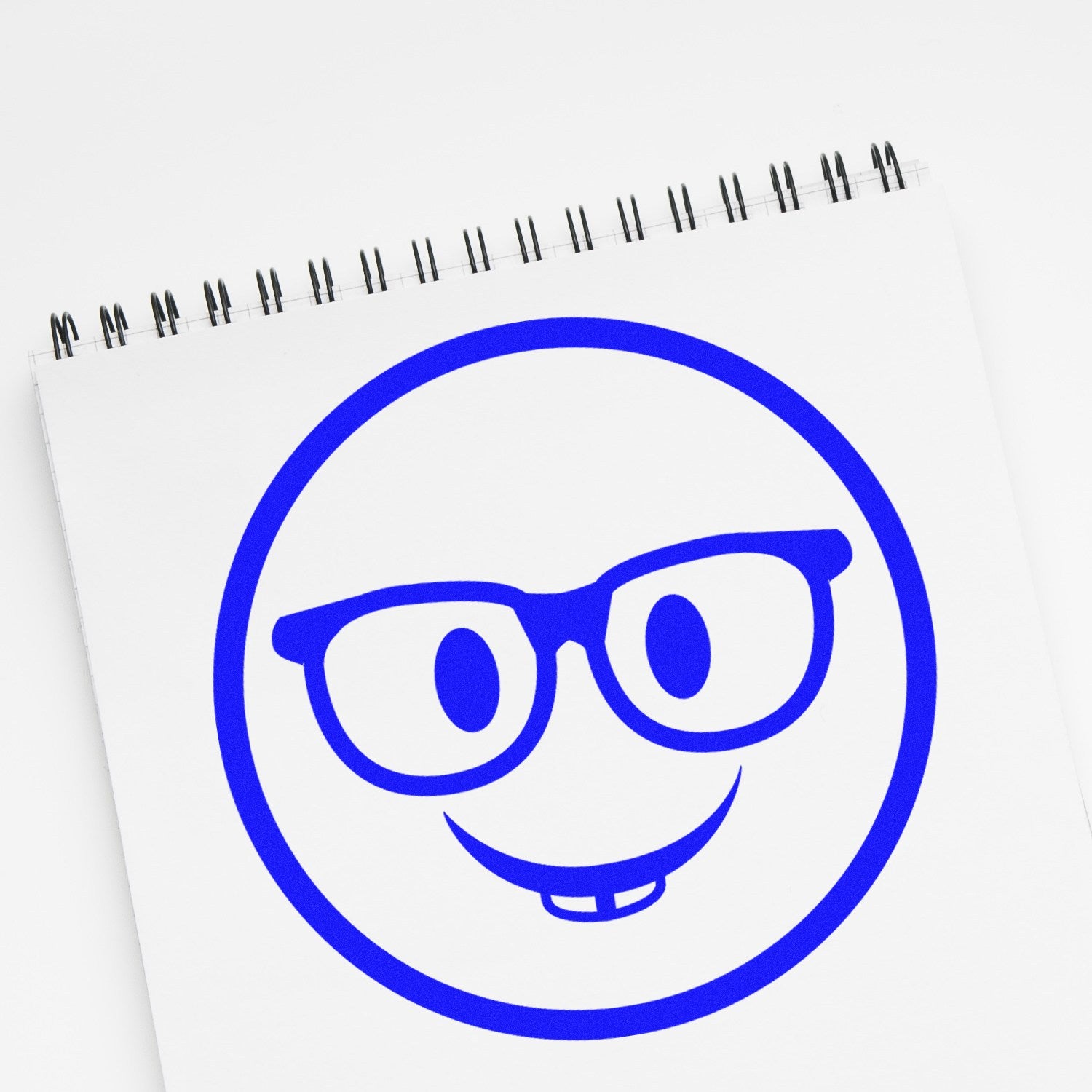 Image of the Self-Inking Wise Guy Smiley Stamp imprint on a spiral notebook, featuring a blue smiley face with glasses and a toothy grin. Perfect for adding fun to your stationery.