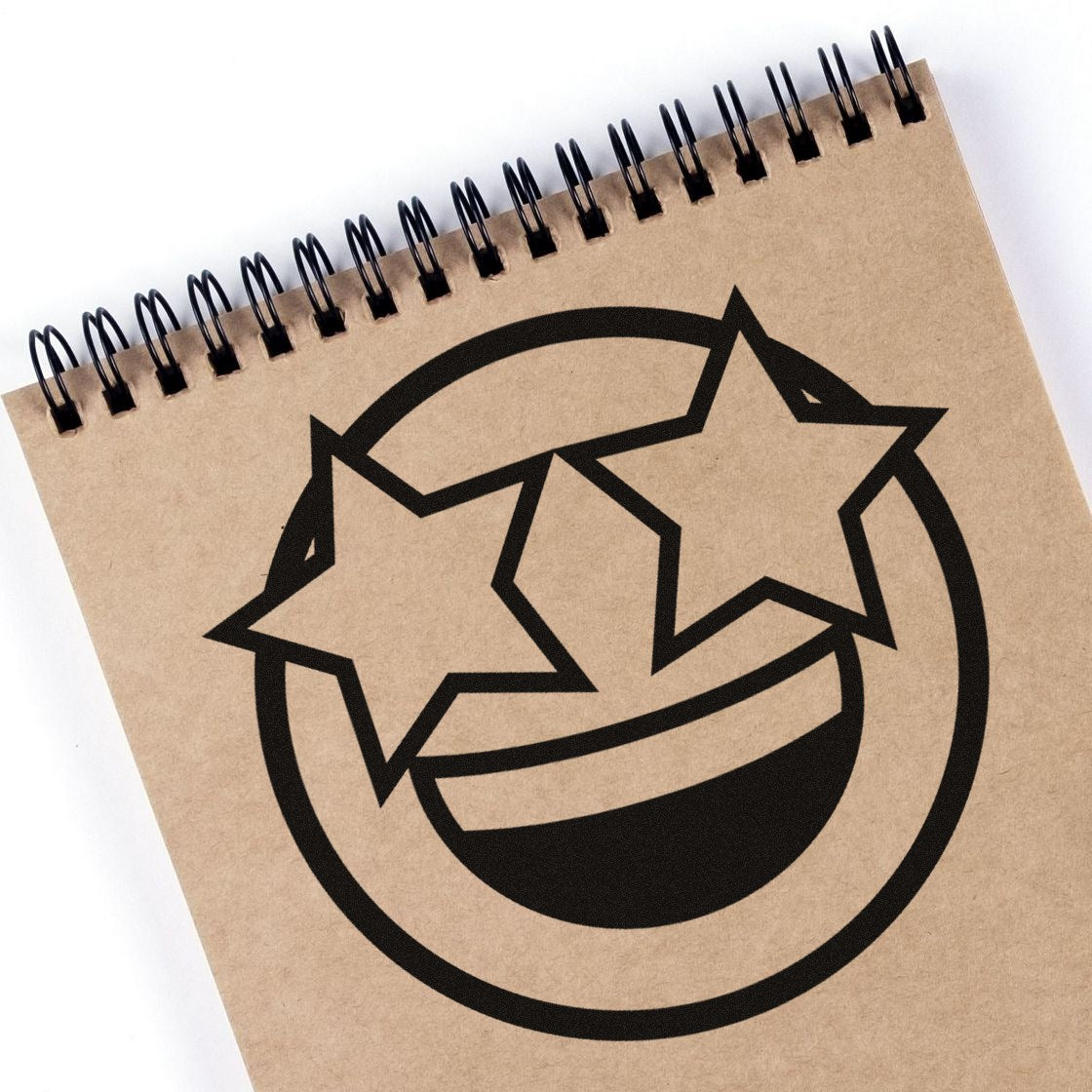 Wood Handle Starry Eyed Emotes Rubber Stamp imprint on notebook, featuring a smiling face with star-shaped eyes. Perfect for crafting and personalizing stationery.