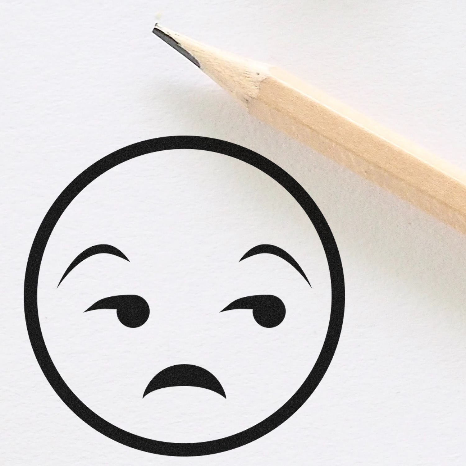 Wood Handle Grumpy Gus Facial Expressions Rubber Stamp showing a skeptical face design, next to a sharpened pencil on white paper. Perfect for adding personality to crafts and stationery.