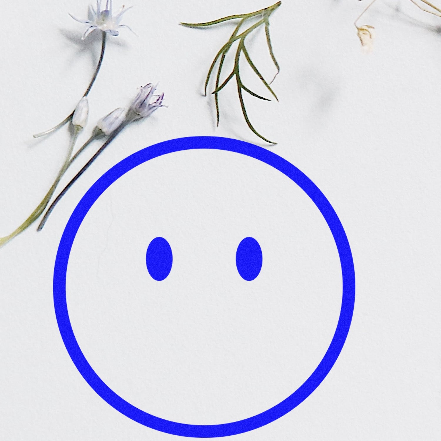 Self-Inking Speechless Sam Emoji Stamp with a blue outline and simple face design, surrounded by delicate flowers on a white background.