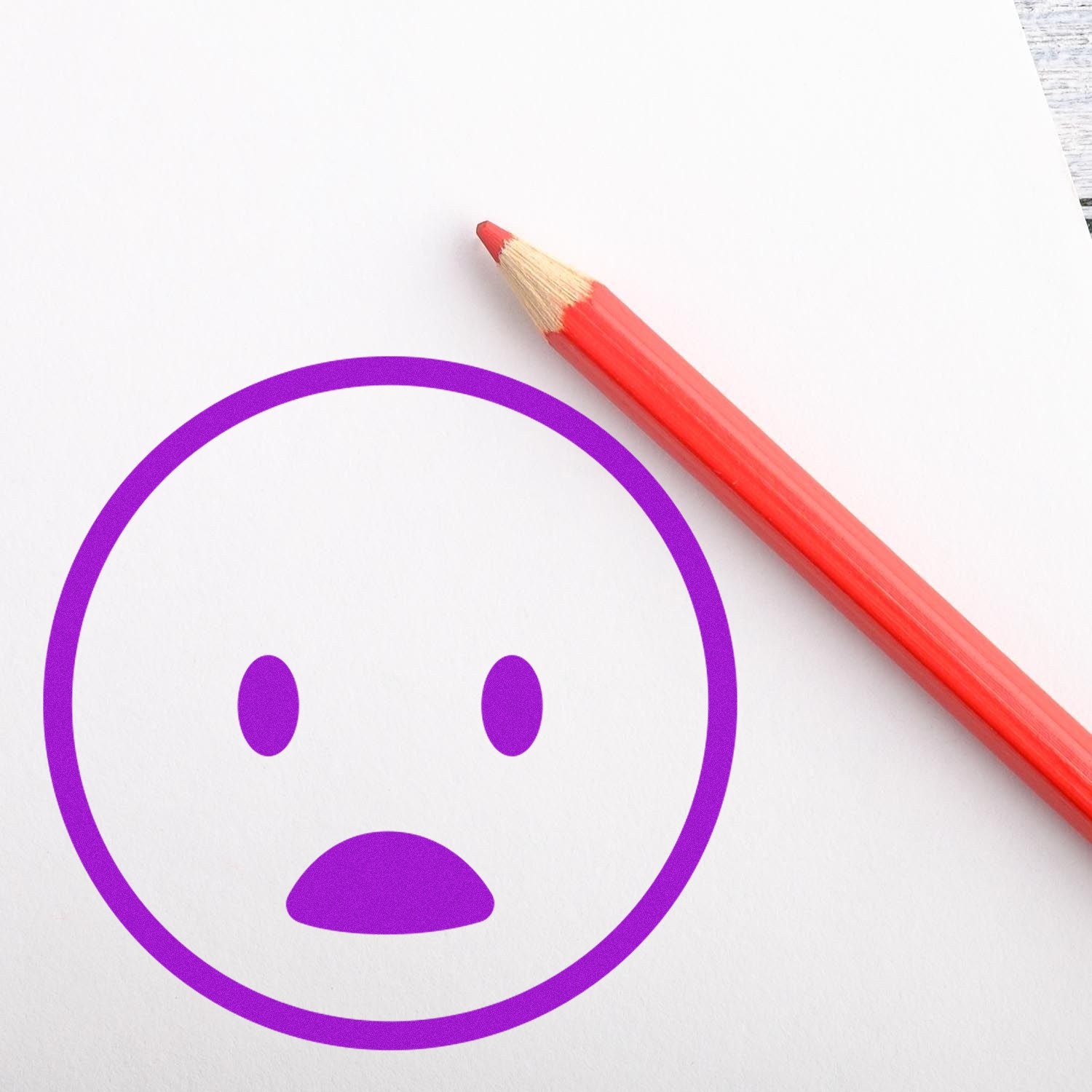 Self-Inking Surprised Smiley Emoji Stamp in purple ink on white paper, next to a red pencil. Perfect for adding fun expressions to documents and crafts.