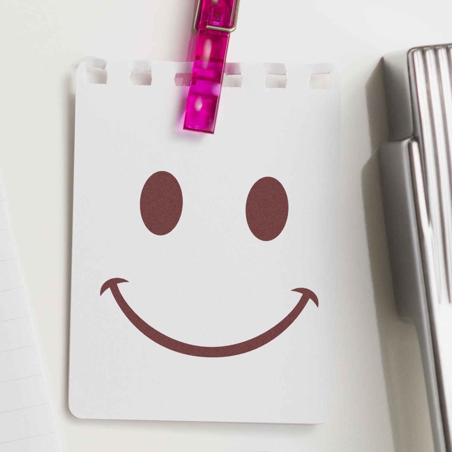 Wood Handle Cheeky Smirk Emoji Rubber Stamp on a notepad, showcasing a playful smirk design. Perfect for adding a fun touch to stationery and crafts.