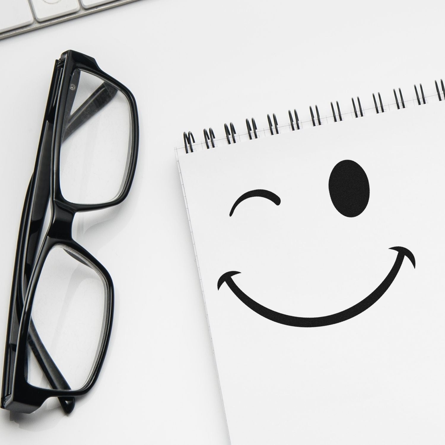 Self-Inking Winky Smirk Emoji Stamp on white paper next to black glasses, showcasing a playful winking face design. Perfect for adding fun to notes and crafts.