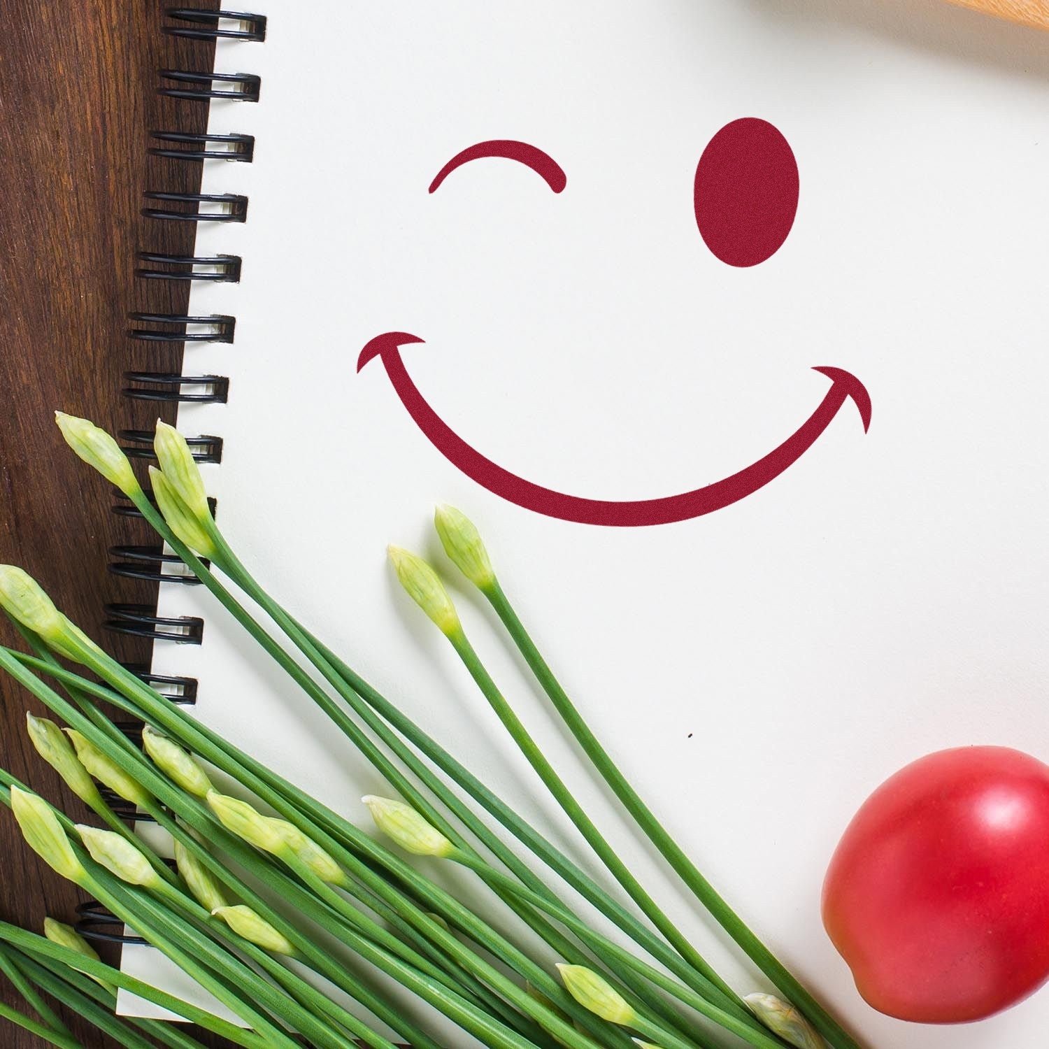 Self-Inking Winky Smirk Emoji Stamp on a spiral notebook, featuring a playful winking face in red ink. Perfect for adding fun to notes and crafts.