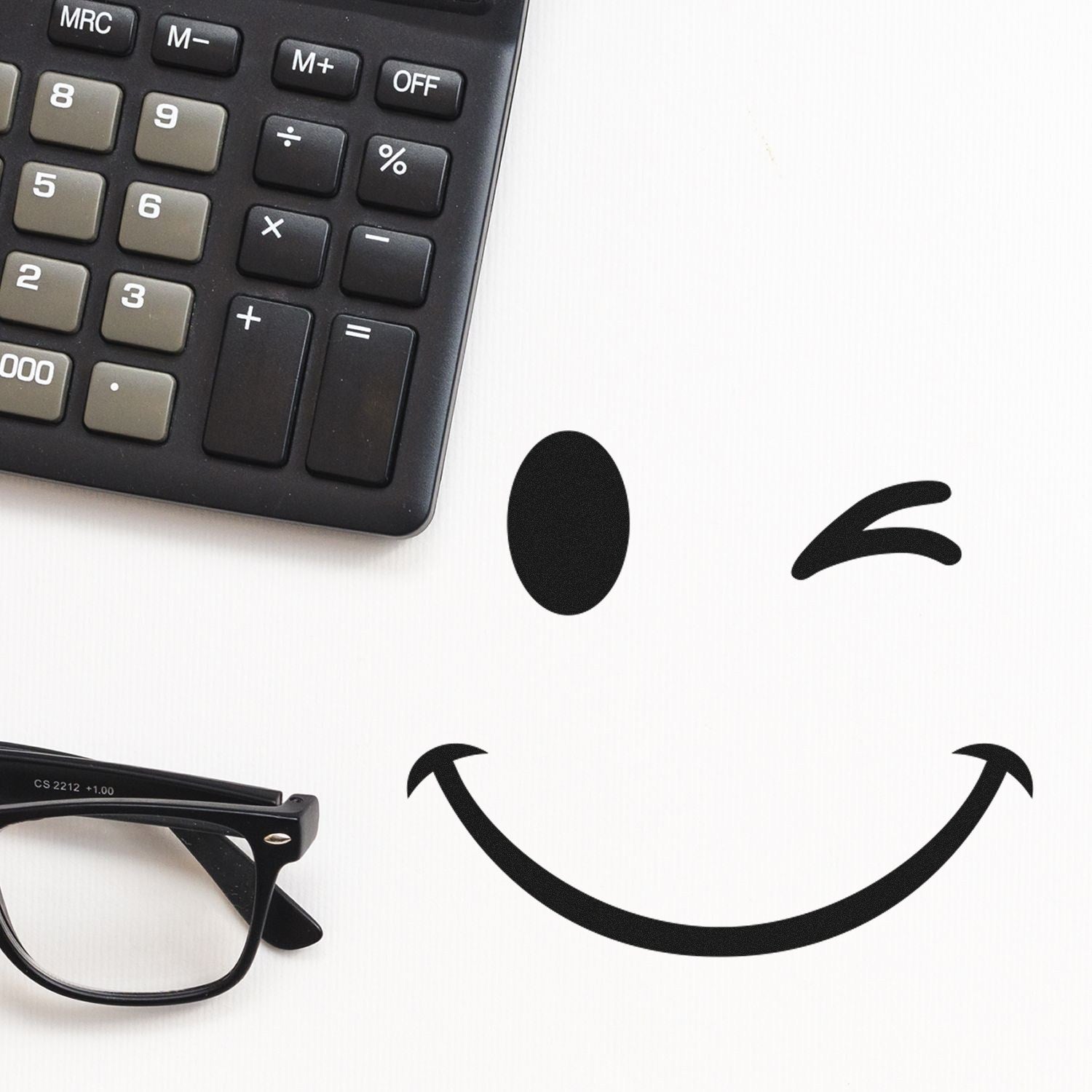 Wood Handle Winky Smiley Emoji Rubber Stamp next to a calculator and glasses, showcasing a playful winking smiley face impression on white paper.