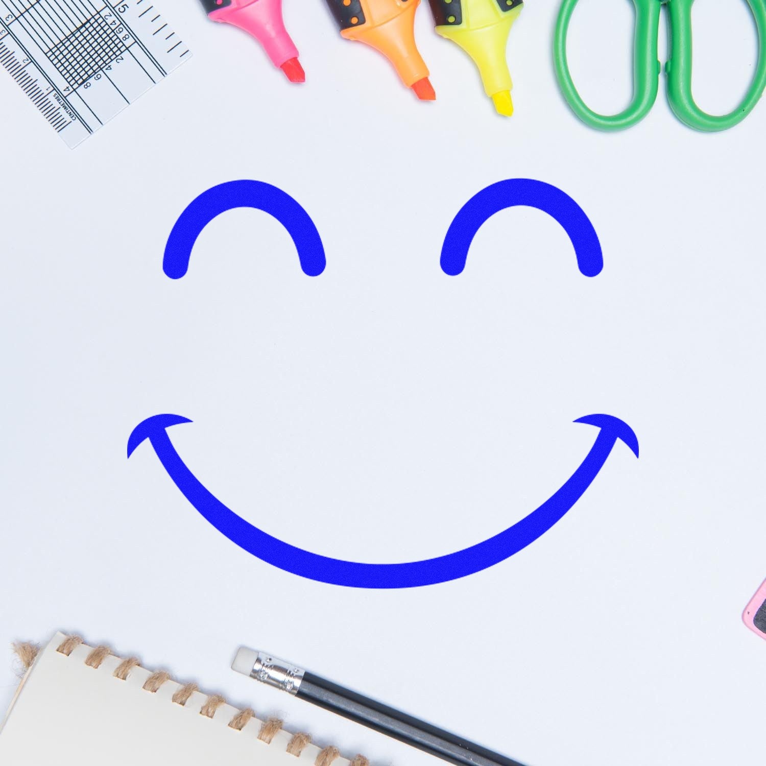 Self-Inking Giggly Smiley Emoji Stamp on white paper, surrounded by colorful highlighters, scissors, and stationery, creating a playful and cheerful atmosphere.