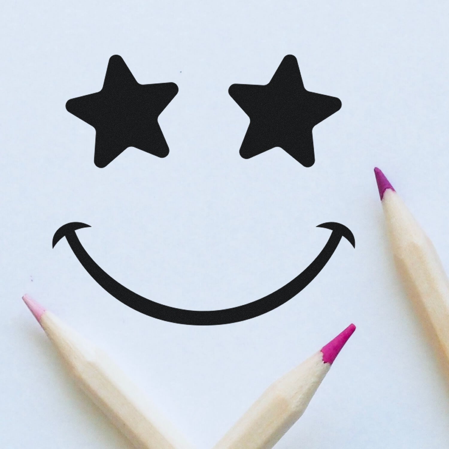 Wood Handle Starstruck Smile Smiley Rubber Stamp creating a star-eyed smiley face on paper, surrounded by colored pencils. Perfect for crafting and stationery enthusiasts.