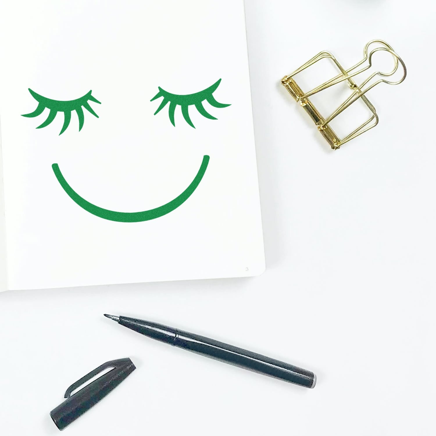 Wood Handle Dreamy Delight Pictogram Rubber Stamp with a smiling face and closed eyes design, shown on white paper. Includes a black pen and gold paper clip nearby.