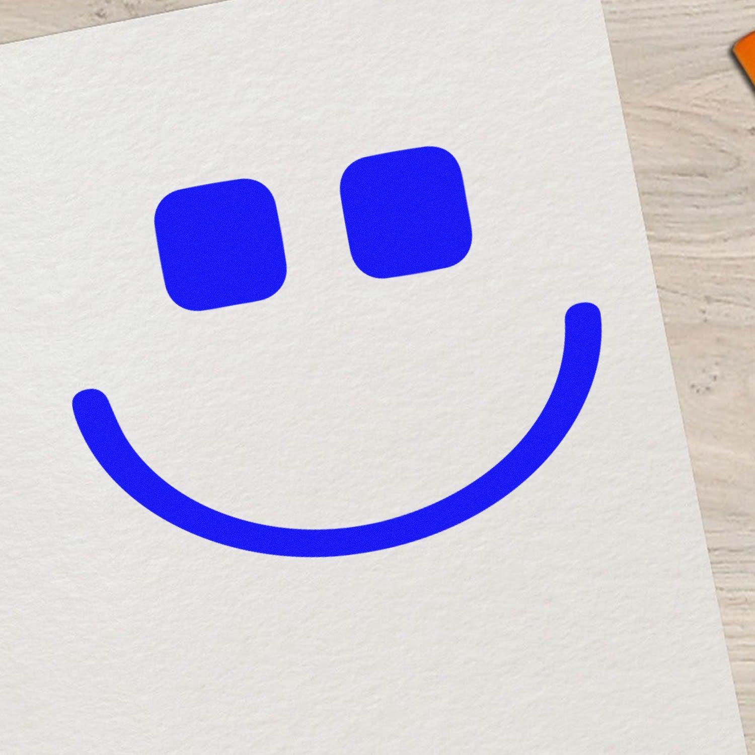 Self-Inking Geeky Grin Emotes Stamp on paper, featuring a bold blue smiley face with square eyes. Perfect for adding a playful touch to notes and crafts.