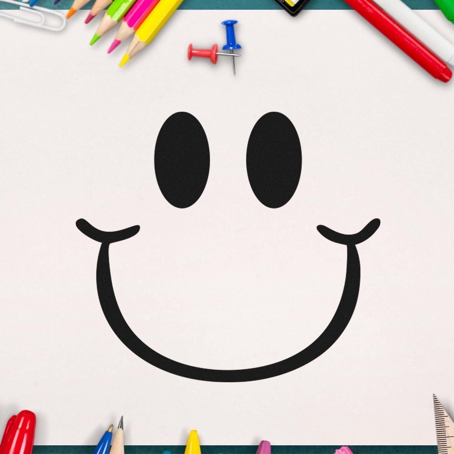 Image of the Self-Inking Playful Smirk Reaction Stamp, featuring a bold black smirk face design on white paper, surrounded by colorful stationery items like pencils and push pins.