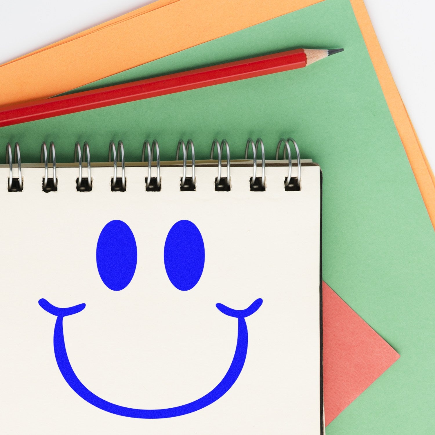 Self-Inking Playful Smirk Reaction Stamp on a notepad with a red pencil, featuring a blue smirk face design. Perfect for adding fun expressions to your notes and documents.