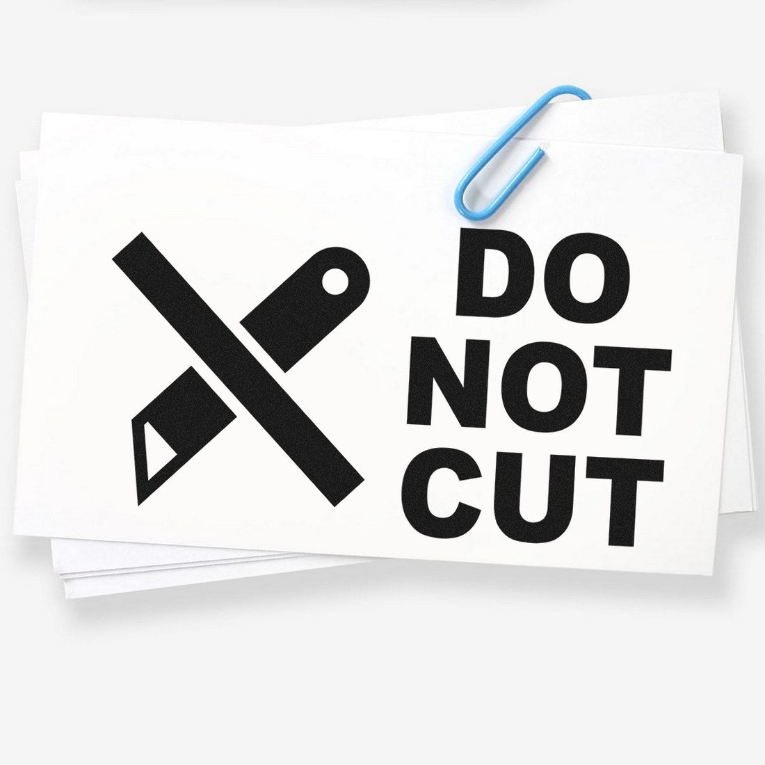 Self-Inking Do Not Cut Symbol Stamp featuring a bold black crossed knife icon and Do Not Cut text on white paper, secured with a blue paperclip. Perfect for labeling and safety warnings.