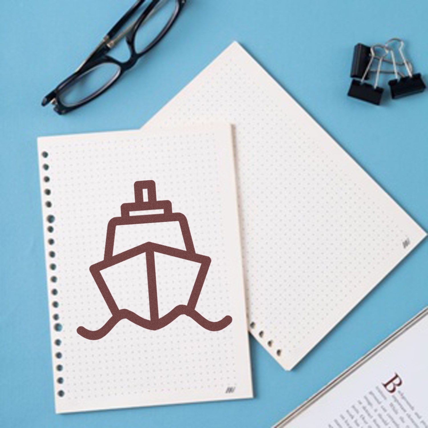 Self-Inking Ships Away Repeat Customer Stamp on dotted paper, featuring a ship design. Includes glasses, binder clips, and a notebook on a blue background.