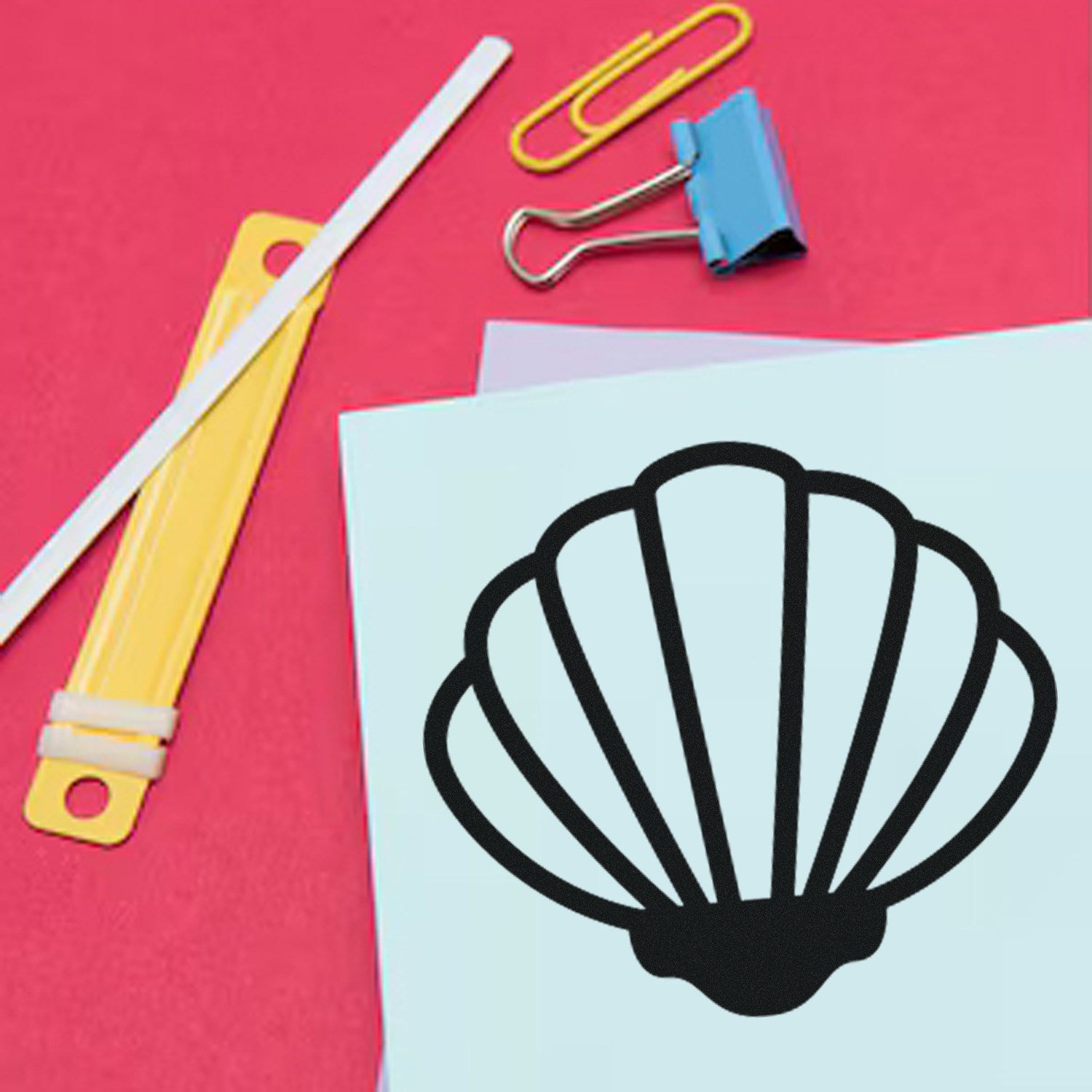 Self-Inking Beach Beauty Membership Stamp featuring a seashell design on a blue card, surrounded by a yellow ruler, paper clips, and a binder clip on a pink background.