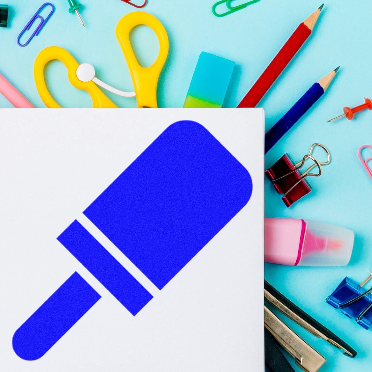 Wood Handle Pop Of Approval Visit Rubber Stamp on a colorful desk with stationery items like scissors, pencils, and paper clips. The stamp features a bold blue design on a white background.