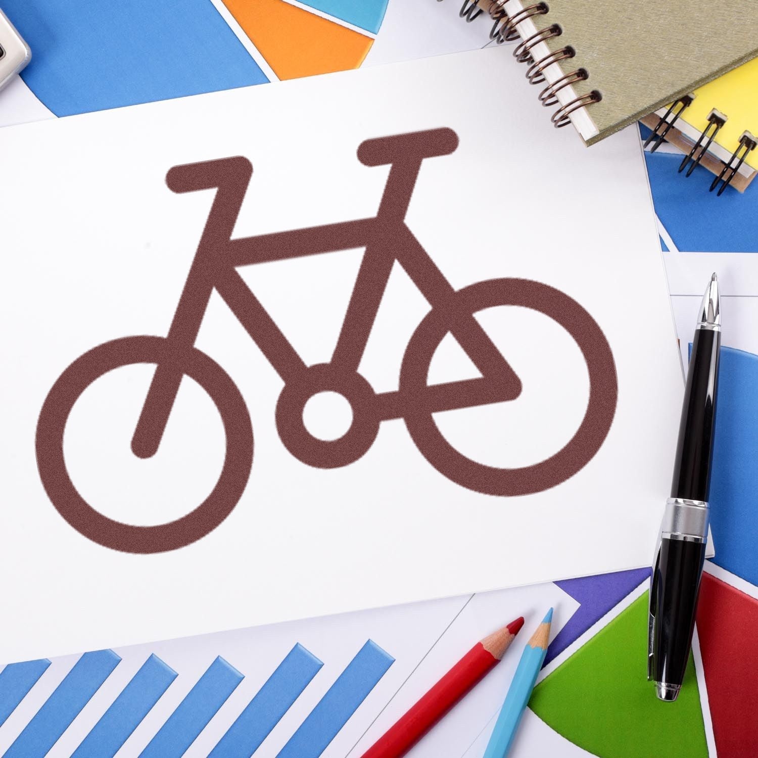 Self-Inking Cycle Of Loyalty Stamp on paper, featuring a brown bicycle design. Surrounded by colorful papers, a pen, and pencils, ideal for creative and office use.