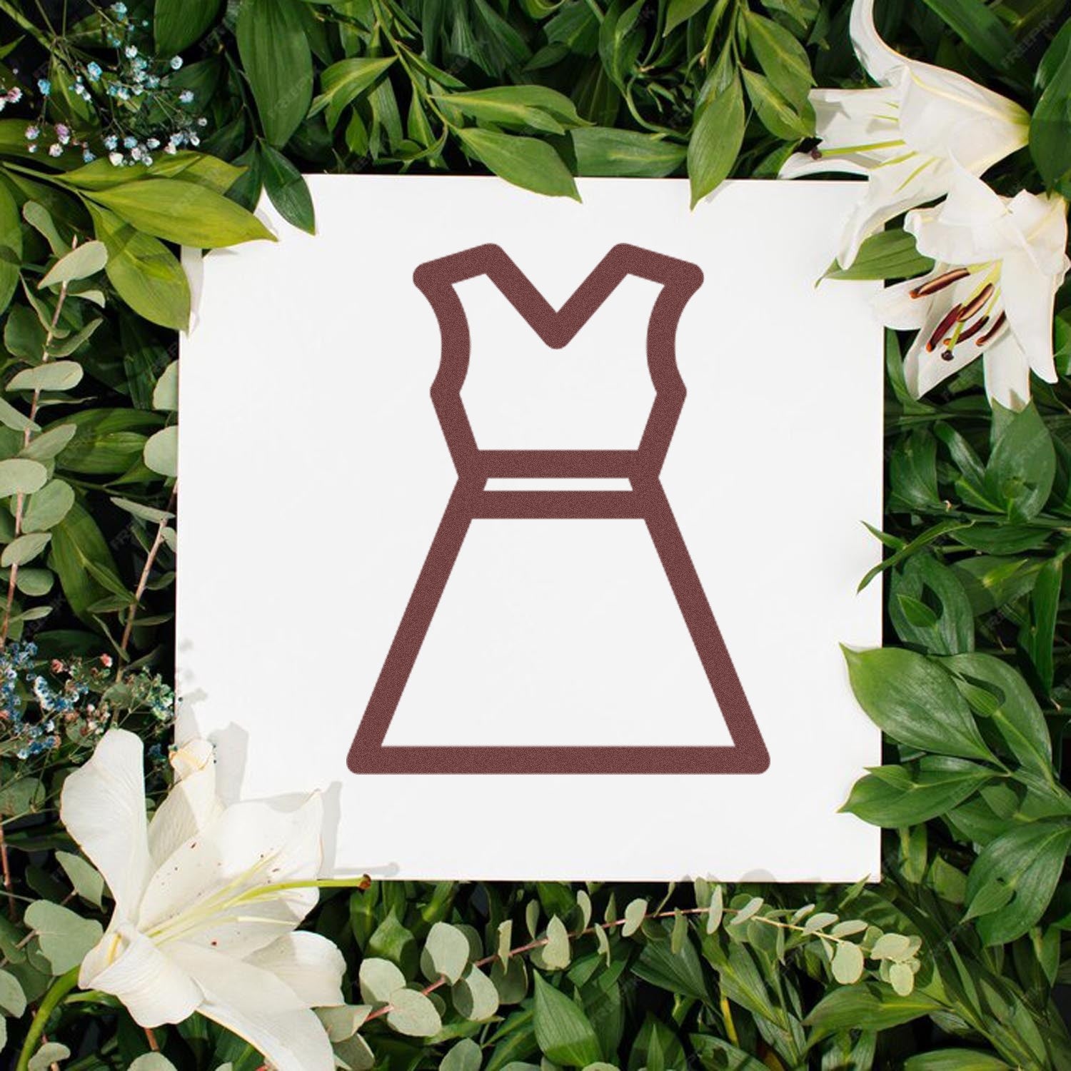 Wood Handle Clothing Punch Card Rubber Stamp on a white background, surrounded by lush green leaves and white lilies, showcasing a dress outline design. Perfect for crafting and DIY projects.