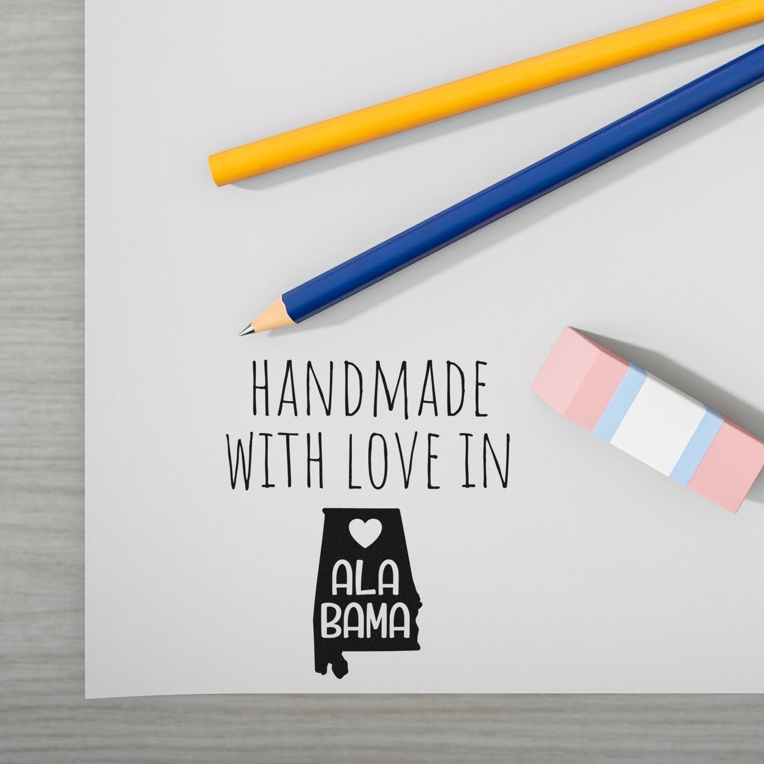 Wood Handle Alabama Handmade with Love Rubber Stamp on paper, featuring a heart and Alabama state outline, alongside colorful pencils and an eraser. Perfect for crafts and personalized projects.