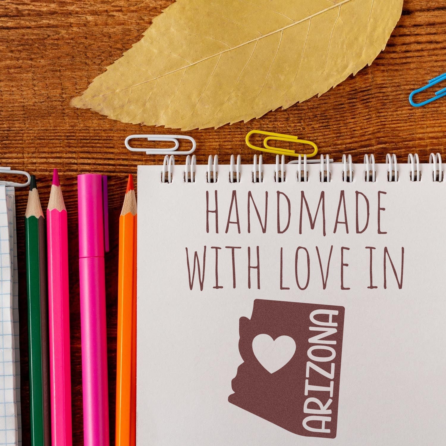 Wood Handle Arizona Handmade with Love Rubber Stamp on notepad, surrounded by colorful pencils and paperclips, showcasing a heart and Arizona state outline. Perfect for crafts and gifts.