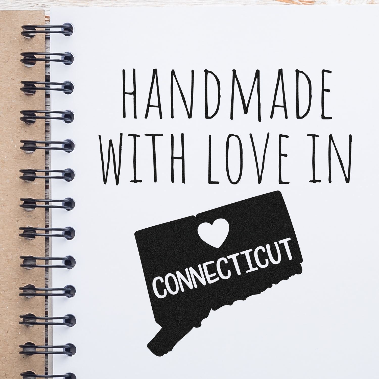 Wood Handle Connecticut Handmade with Love Rubber Stamp on a spiral notebook, featuring a heart and state outline design. Perfect for crafts and personalized projects.